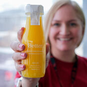 A woman holds a bottle of bright yellow juice up to the camera.